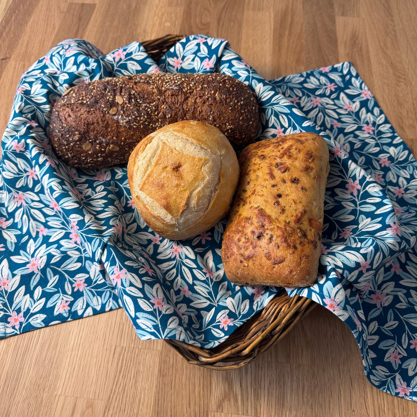 Three loaves of bread in a basket with a floral-patterned cloth on a wooden surface