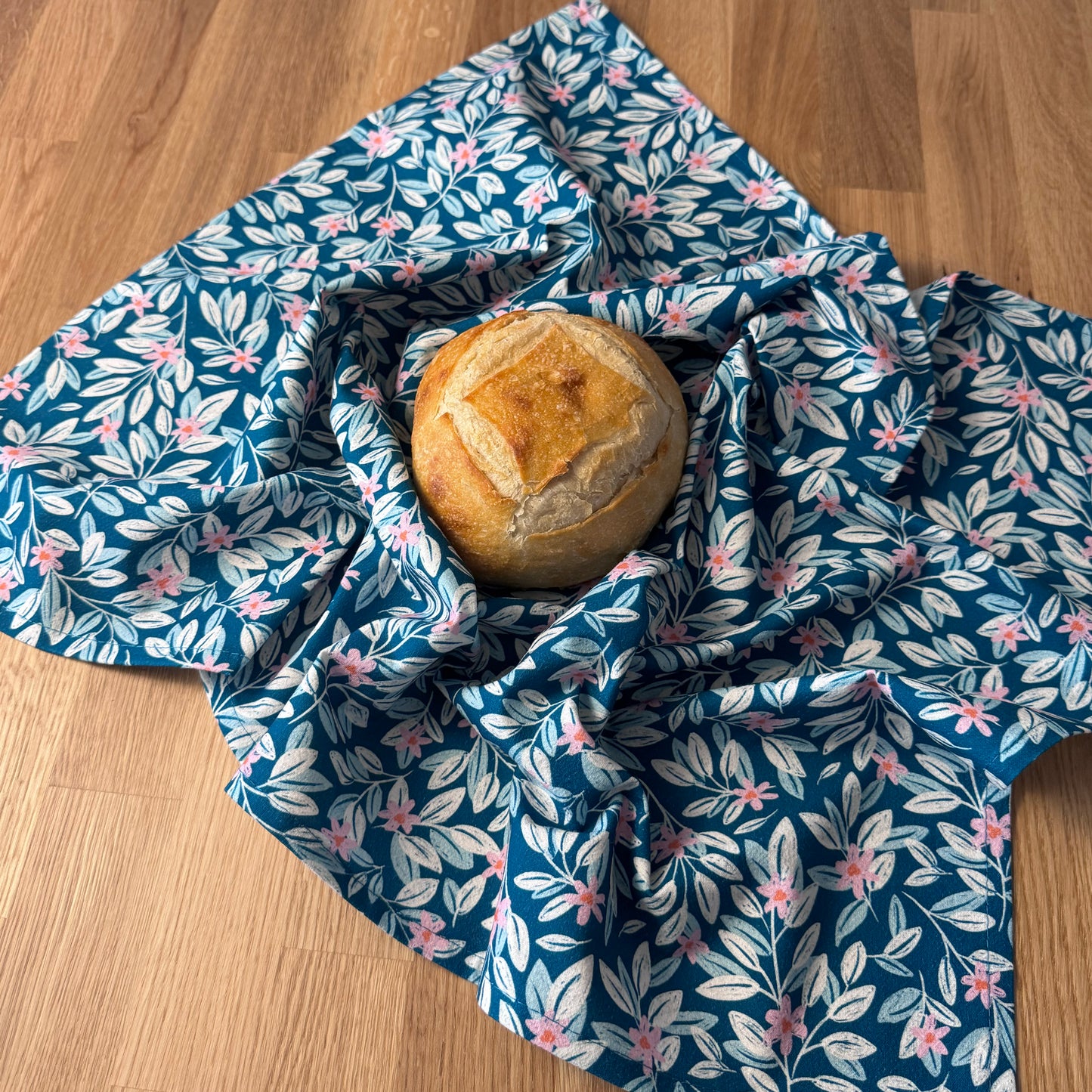 Loaf of bread wrapped in a blue floral patterned cloth on a wooden surface