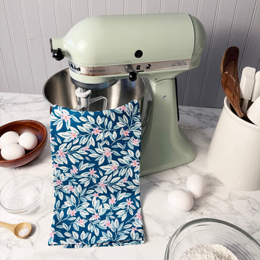 Kitchen scene with a green stand mixer, floral-patterned towel, and kitchen utensils on a white countertop.