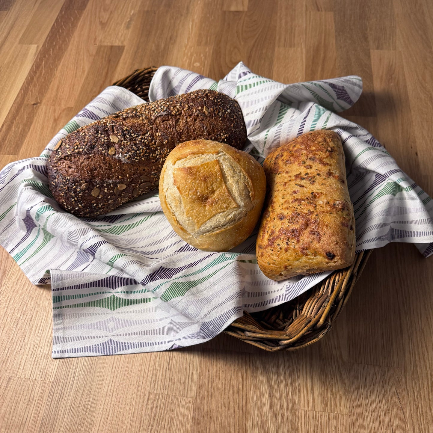 Three loaves of bread in a basket with a striped cloth on a wooden surface