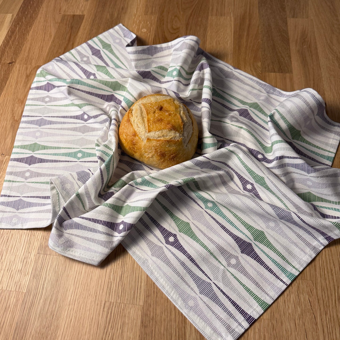 Loaf of bread wrapped in a patterned cloth on a wooden surface