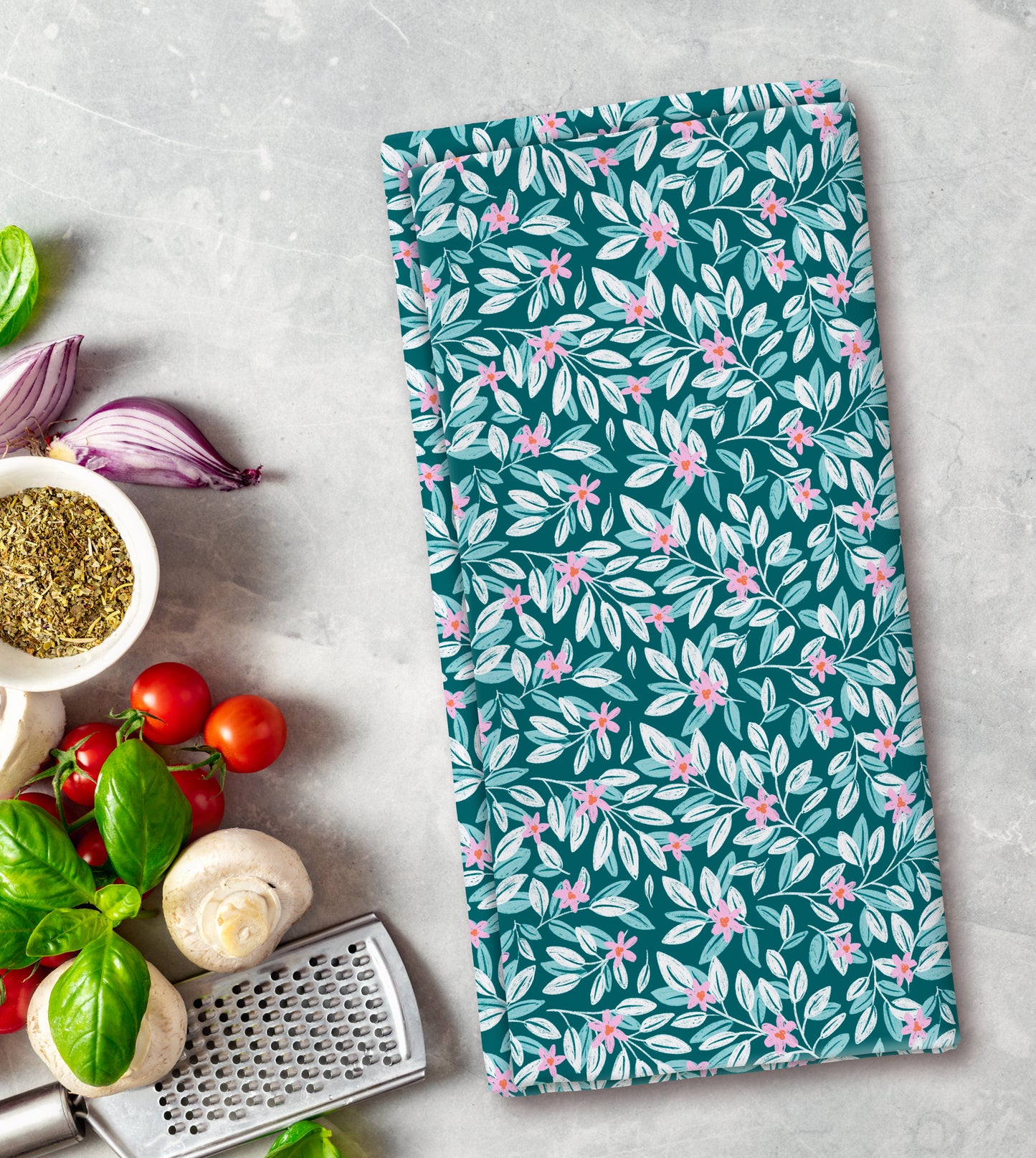 Floral patterned towel on a kitchen counter with vegetables and a grater.