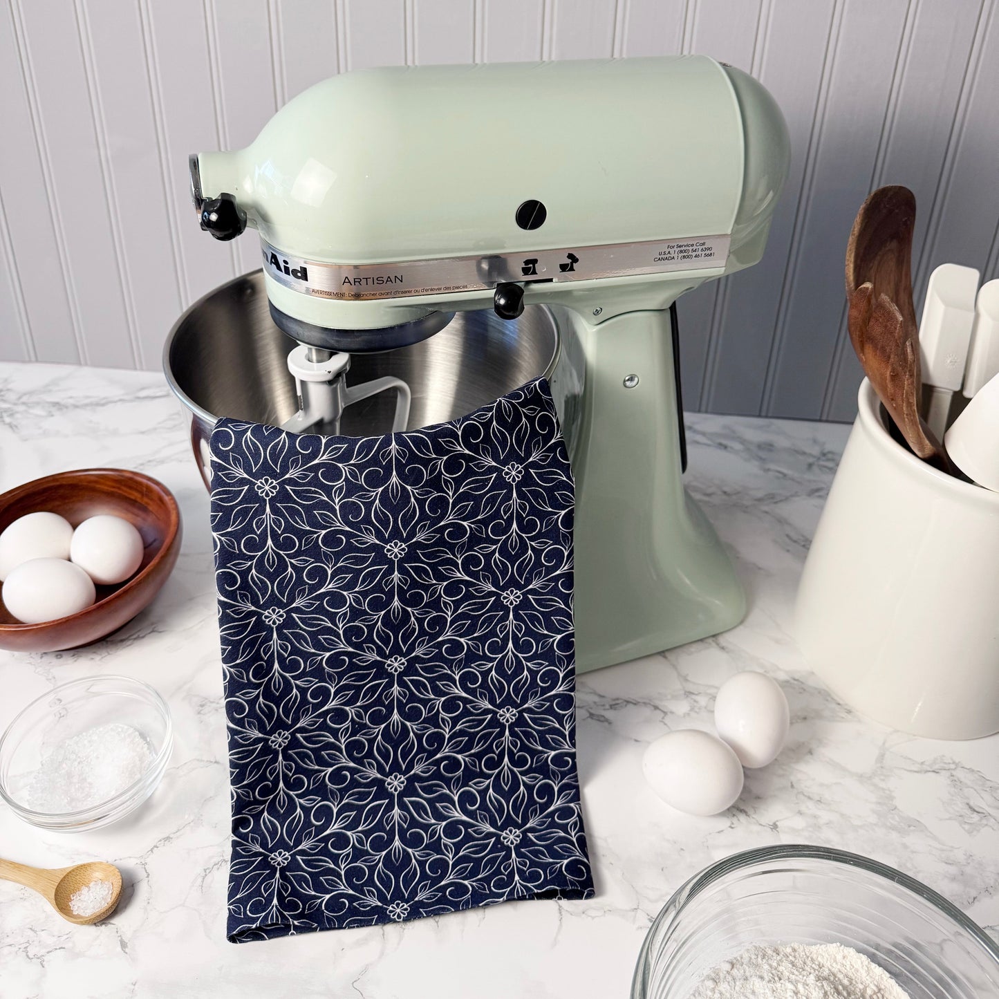 Kitchen scene with a green stand mixer, blue patterned towel, and kitchen utensils on a white countertop.