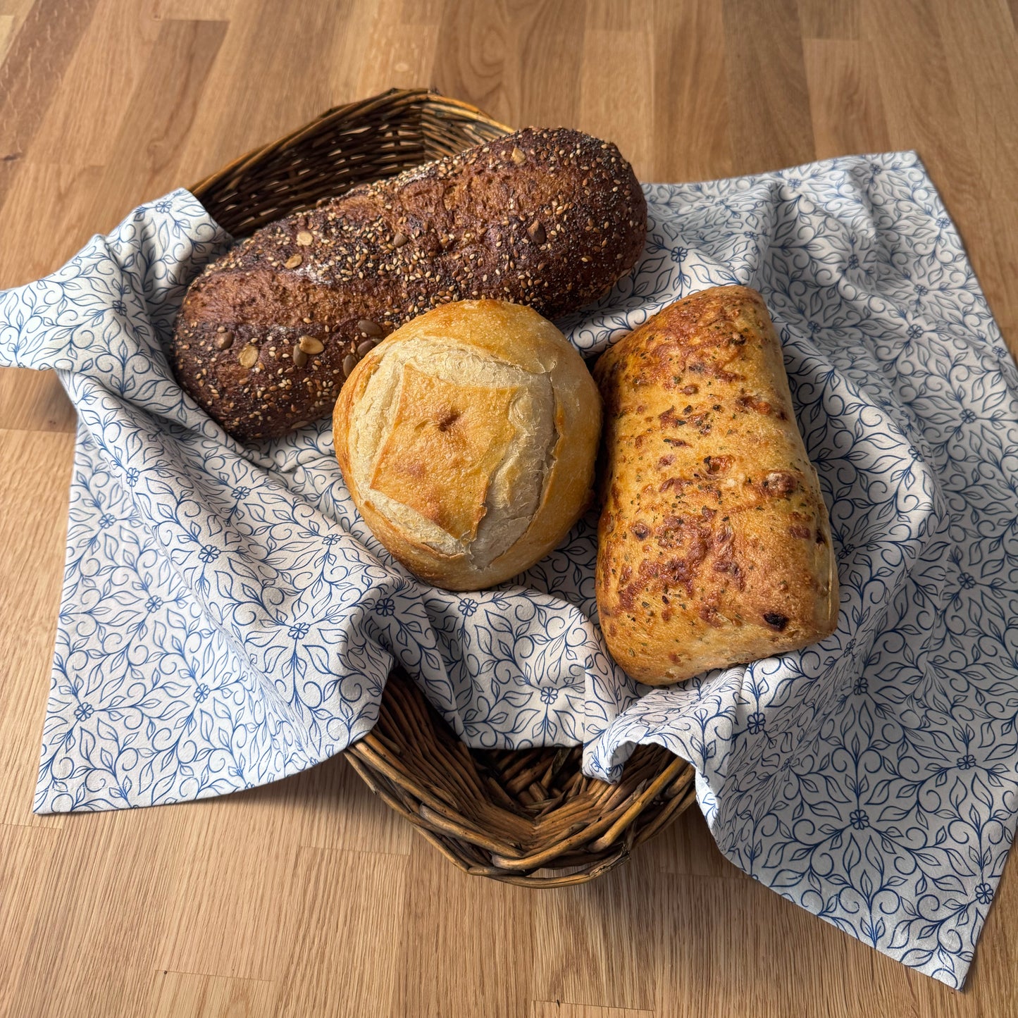 Three loaves of bread in a basket with a patterned cloth on a wooden surface
