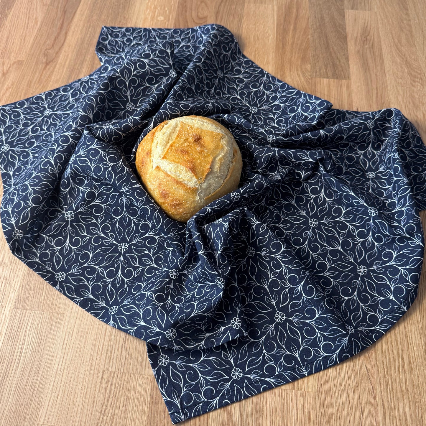 Loaf of bread wrapped in a blue patterned cloth on a wooden surface