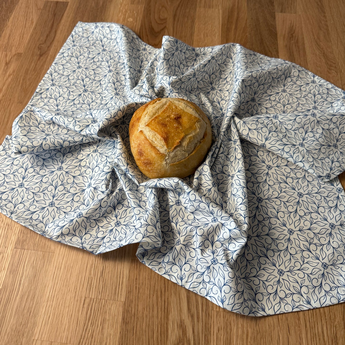 Loaf of bread wrapped in a floral-patterned cloth on a wooden surface