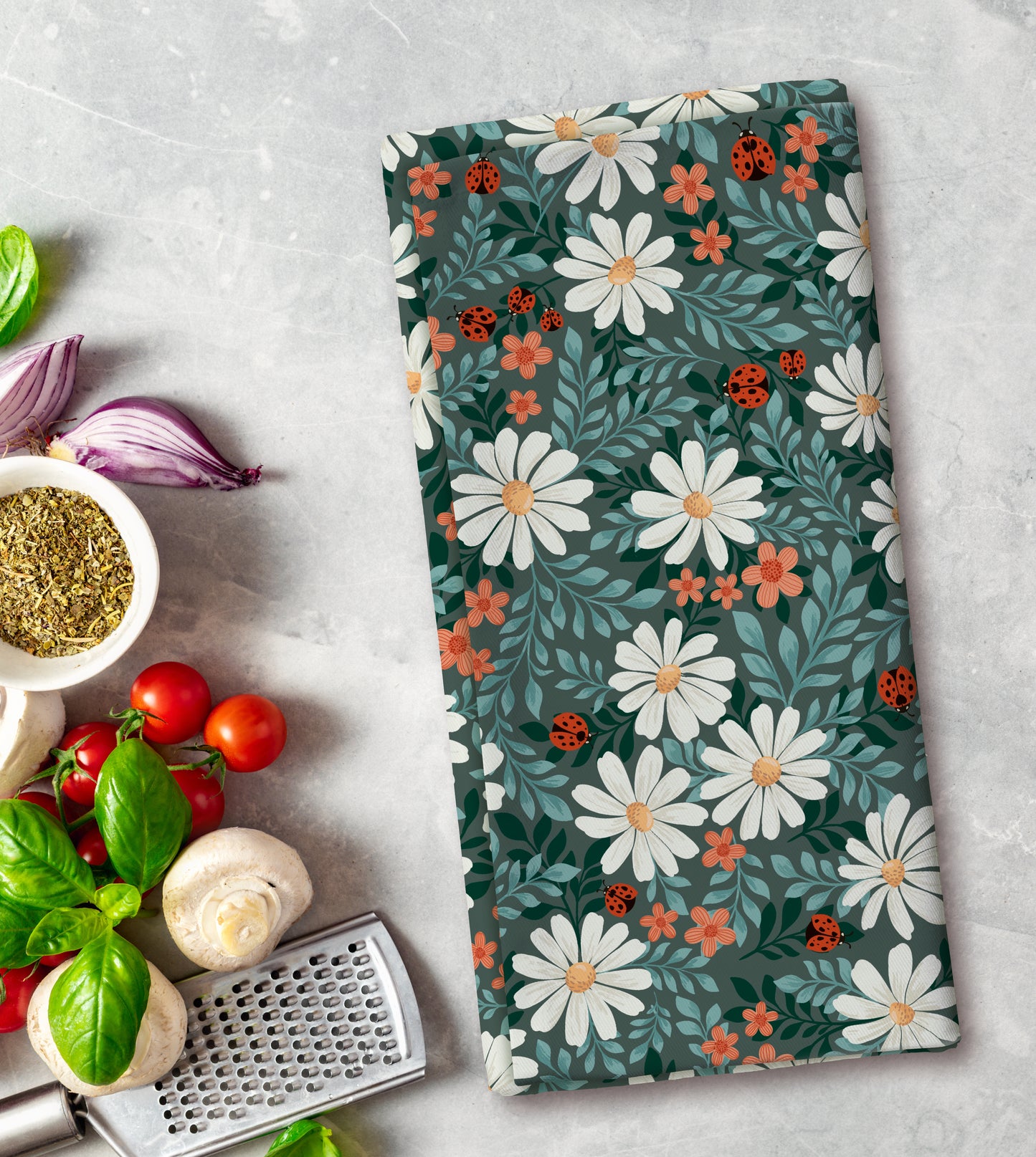 Floral patterned towel on a kitchen counter with vegetables and a grater.