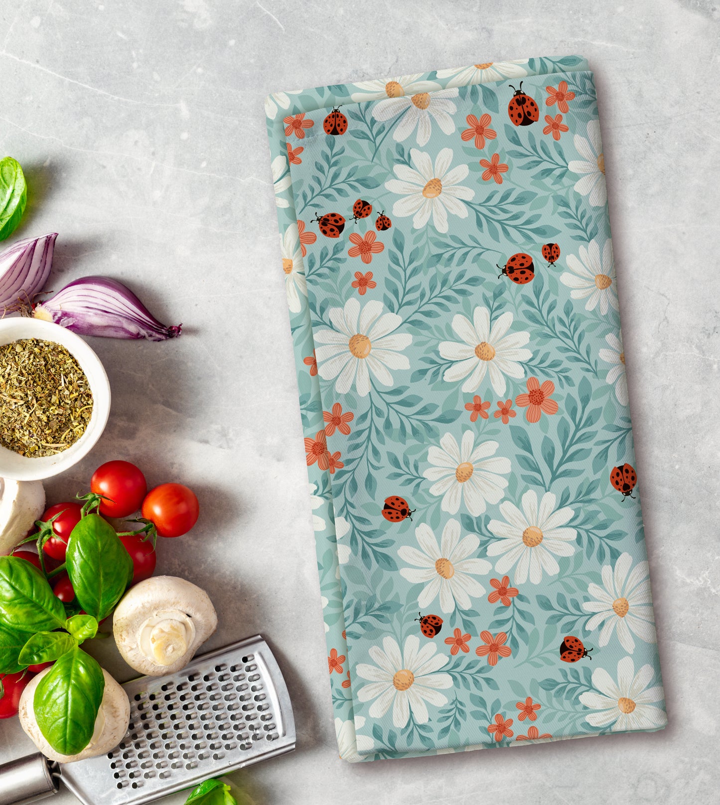 Floral patterned towel with ladybugs on a kitchen counter with vegetables and a grater.