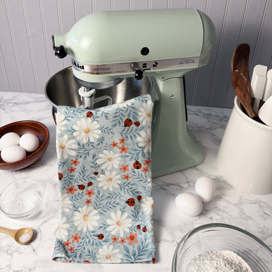 Kitchen scene with a green stand mixer, floral towel, and kitchen utensils on a marble countertop.