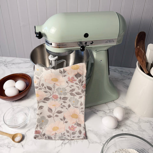 Kitchen scene with a green stand mixer, floral towel, eggs, and kitchen utensils on a marble countertop.