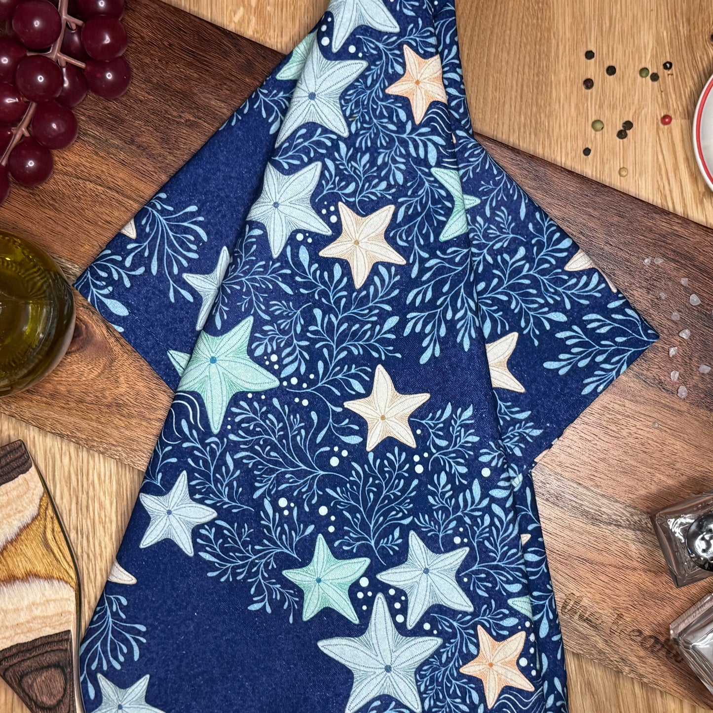 A blue and white tea towel with starfish and marine life patterns, displayed on a wooden surface.