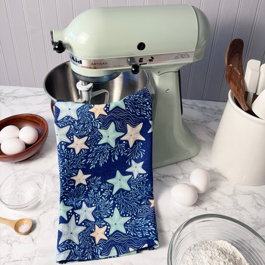 Kitchen stand mixer with a blue star-patterned towel draped over it, on a kitchen counter.
