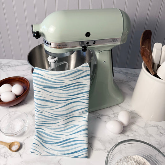 Green KitchenAid stand mixer on a marble countertop with eggs and a towel.