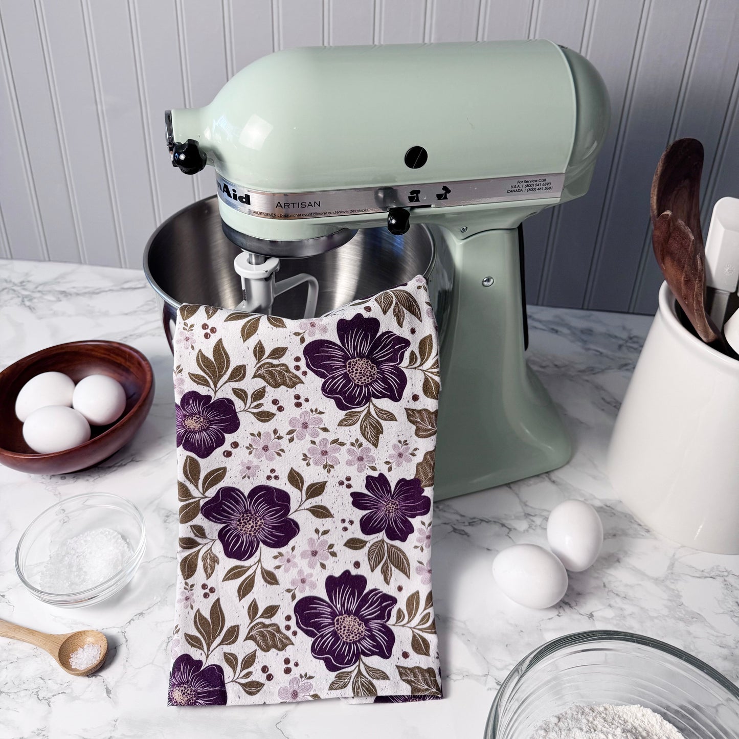Kitchen scene with a mixer, eggs, and a floral-patterned towel on a countertop.