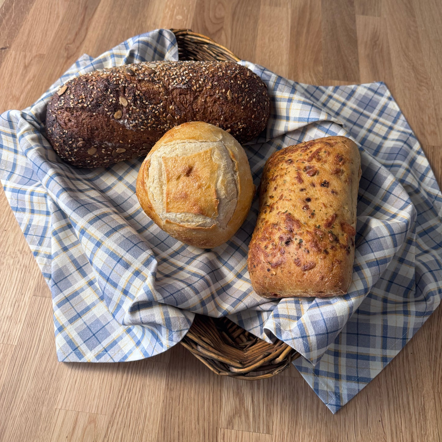 Three loaves of bread in a basket with a blue checkered cloth on a wooden surface