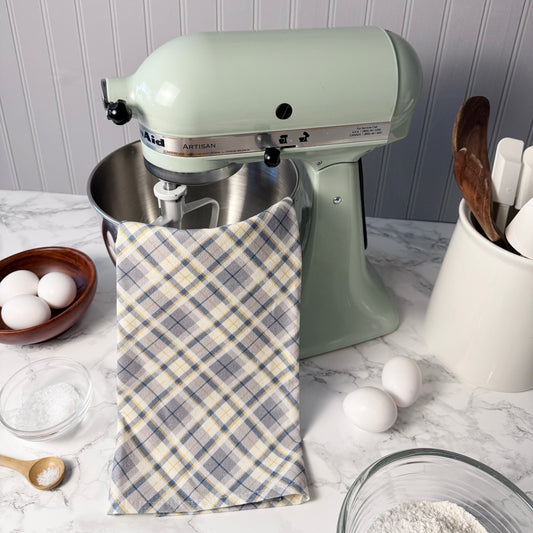 Kitchen scene with a green stand mixer, plaid towel, eggs, and kitchen utensils on a marble countertop.