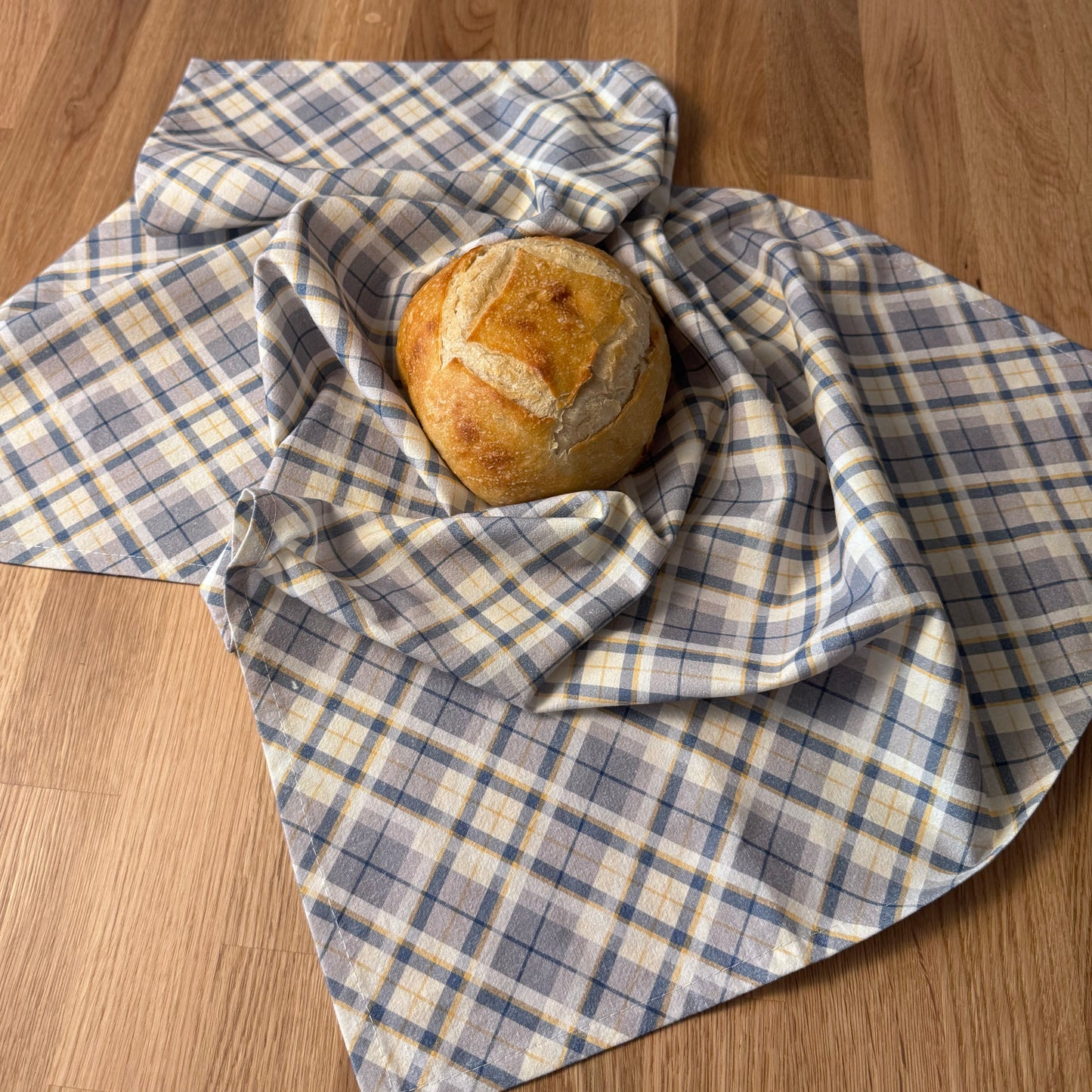 Loaf of bread wrapped in a blue and white checkered towel on a wooden surface