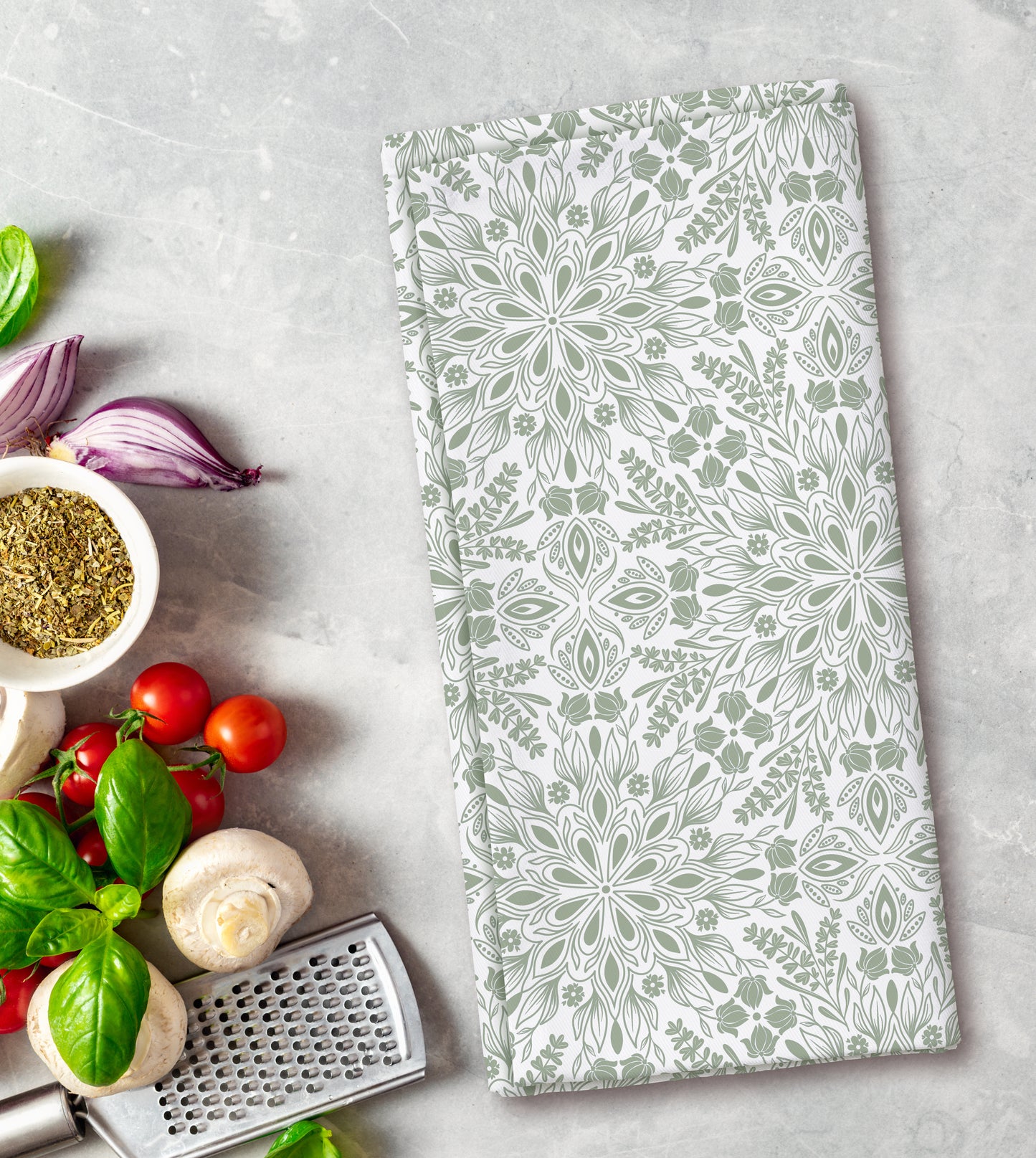Floral patterned kitchen towel on a gray surface with fresh herbs and vegetables.