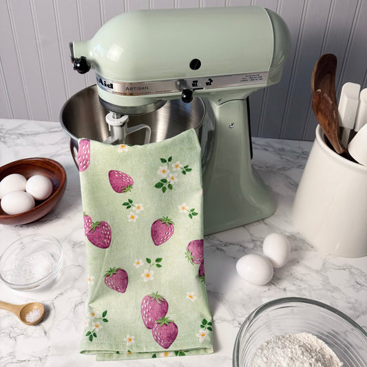 Green kitchen towel with strawberry pattern draped over a stand mixer on a kitchen counter.