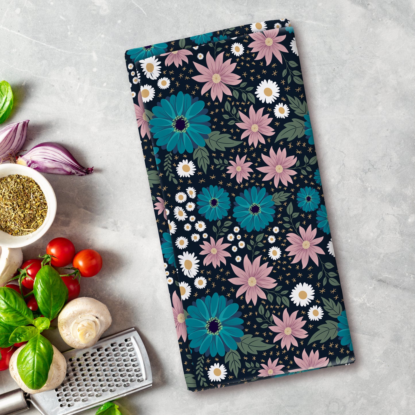 Floral patterned towel on a kitchen counter with vegetables and a grater.
