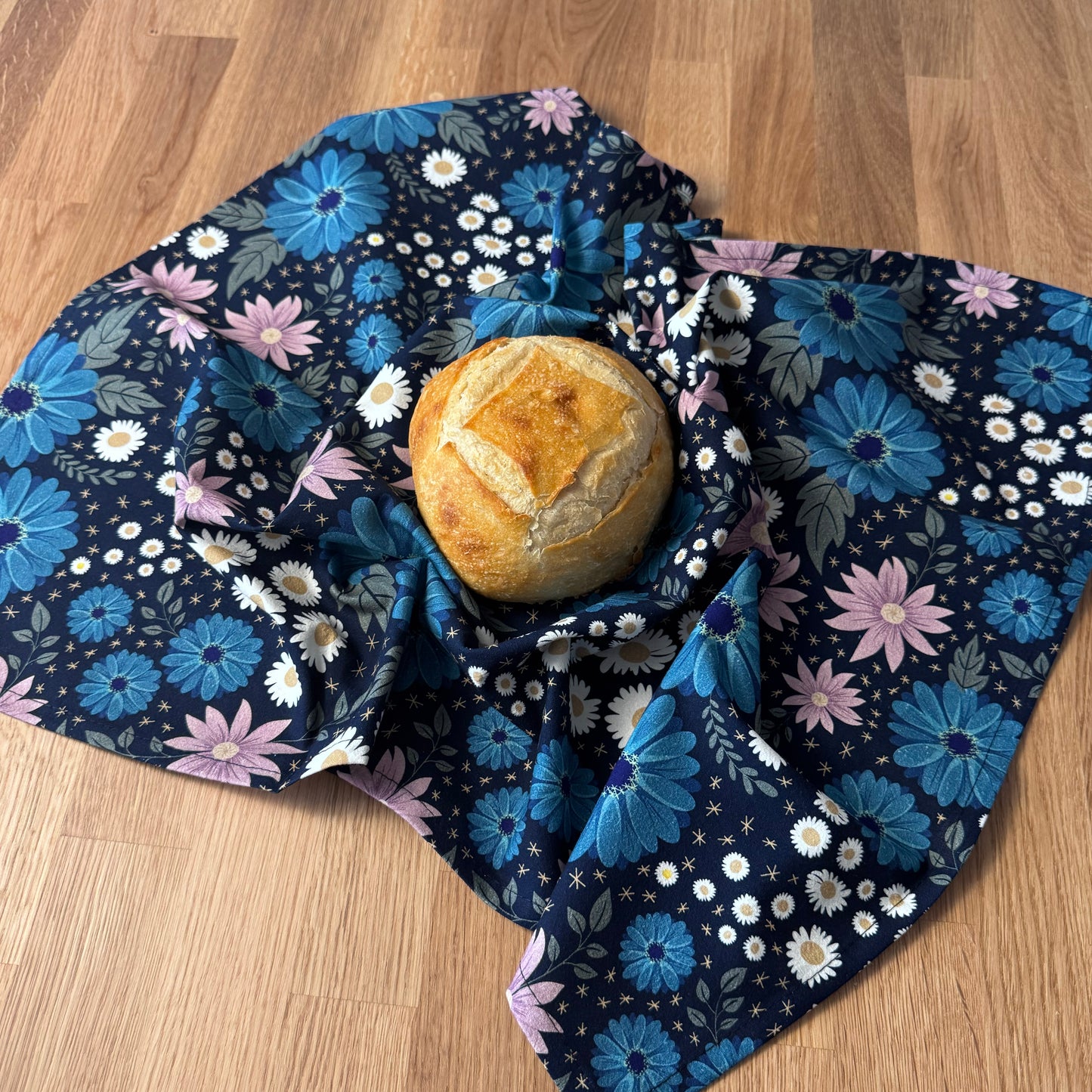 Loaf of bread wrapped in a floral-patterned cloth on a wooden surface
