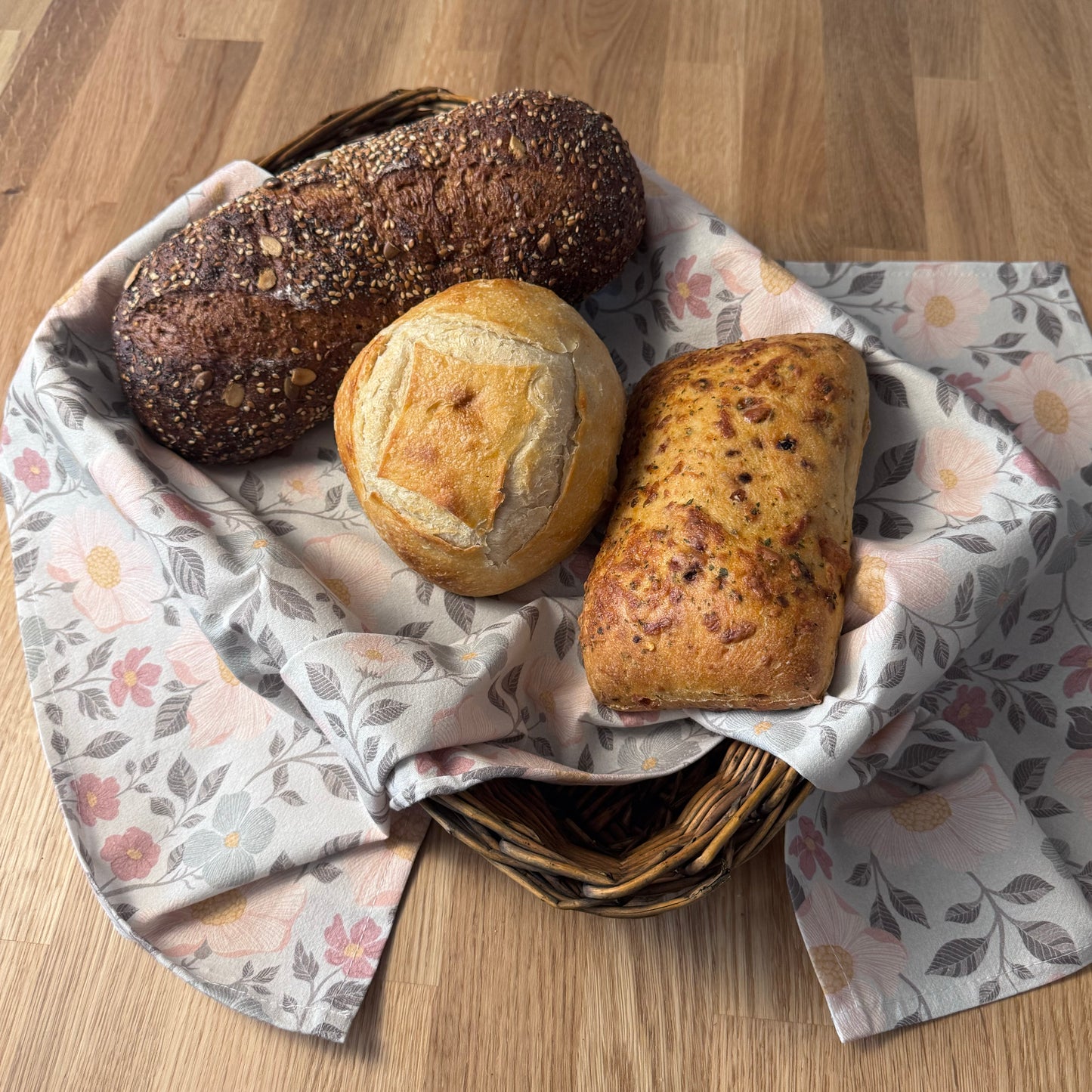 Three loaves of bread in a basket with a floral-patterned cloth on a wooden surface