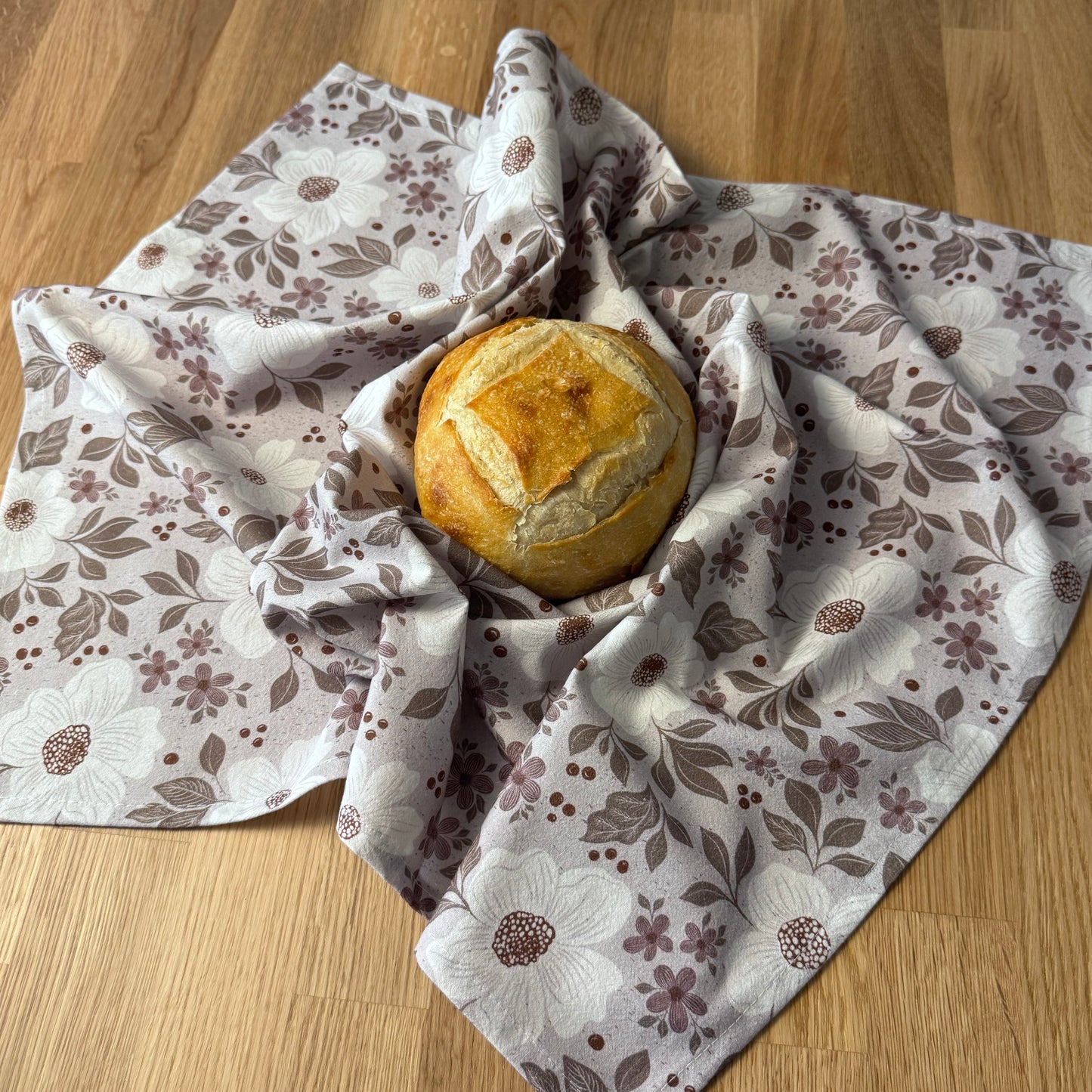 Loaf of bread wrapped in a floral-patterned cloth on a wooden surface