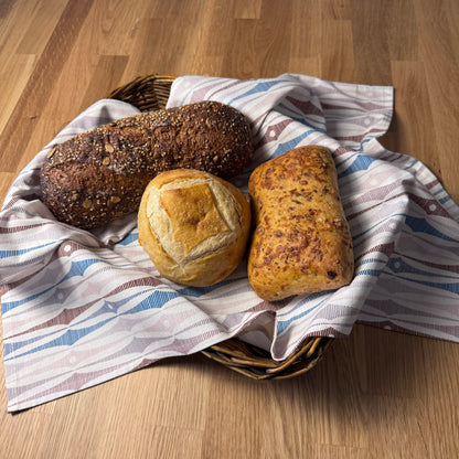Three loaves of bread in a basket on a wooden surface with a patterned cloth.