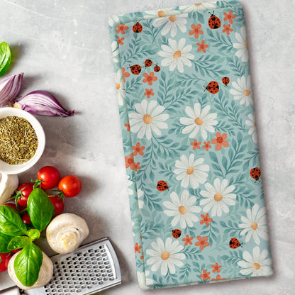 Floral patterned towel with ladybugs on a kitchen counter with vegetables and a grater.