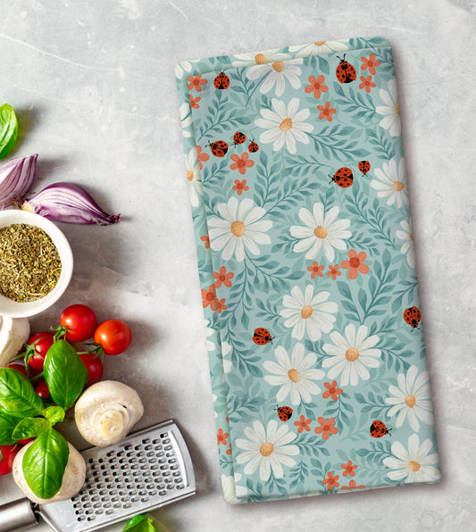 Floral patterned towel with ladybugs on a kitchen counter with vegetables and a grater.