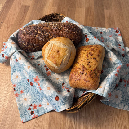 Three loaves of bread in a wicker basket on a floral cloth with a wooden background