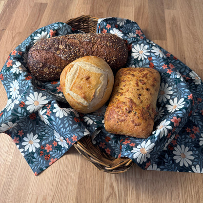Three loaves of bread in a basket lined with floral fabric on a wooden surface