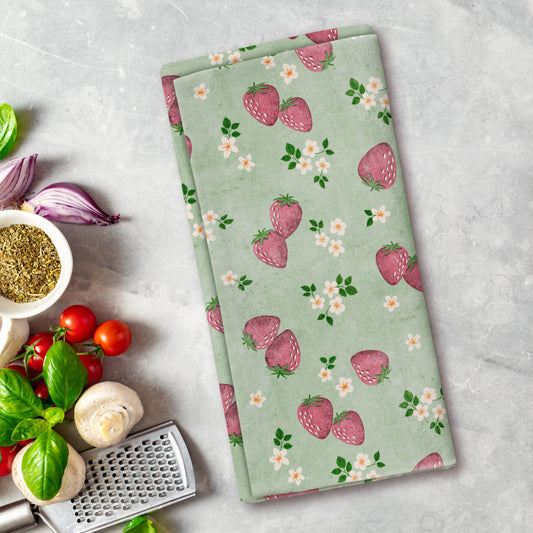 Green kitchen towel with strawberry pattern on a gray surface with vegetables and a grater.